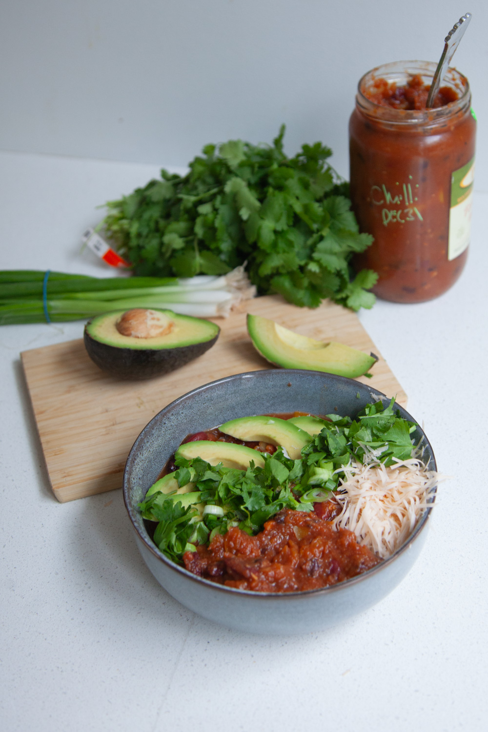 bowl filled with chilli with avocados, green onions and cilantro in the background