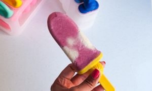 Red and white layer popsicle held by a hand with painted nails