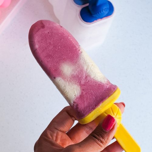 Red and white layer popsicle held by a hand with painted nails